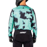 Rear view of a person wearing a long-sleeve athletic jersey with a mint green and black tie-dye pattern, paired with black LEATT riding pants and gloves, on a white background.
